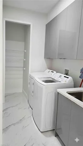 Laundry room with washing machine and dryer, light marble finish flooring, and cabinet space