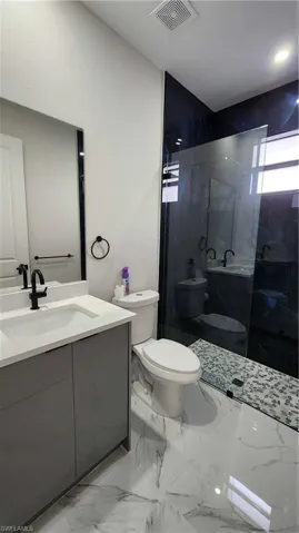Full bathroom featuring vanity, a marble finish shower, and light marble finish flooring