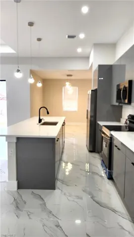 Kitchen with gray cabinetry, range with electric stovetop, decorative light fixtures, stainless steel microwave, and modern cabinets