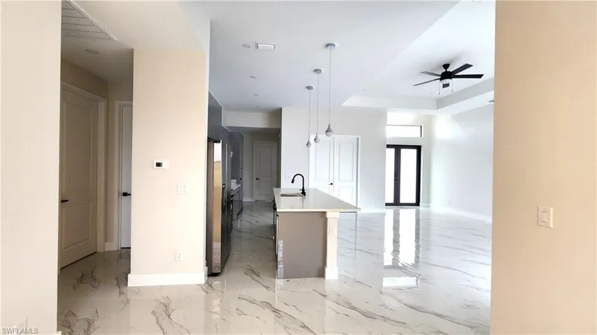 Kitchen featuring open floor plan, pendant lighting, a ceiling fan, a kitchen island with sink, and a raised ceiling