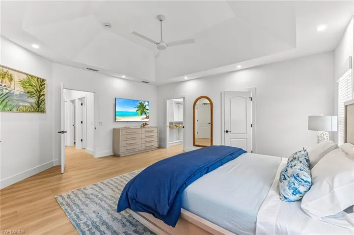 Bedroom featuring a raised ceiling, light wood-style floors, a ceiling fan, recessed lighting, and connected bathroom