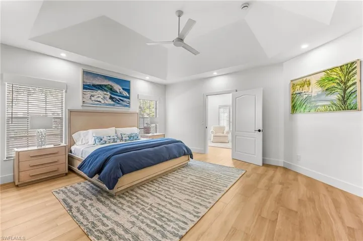 Bedroom with a tray ceiling, light wood-style floors, ceiling fan, recessed lighting, and ensuite bathroom