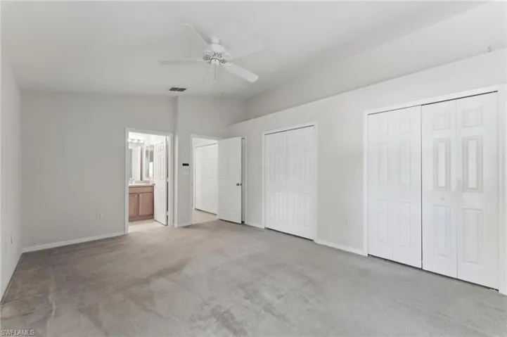 Unfurnished bedroom with connected bathroom, two closets, light carpet, baseboards, and lofted ceiling