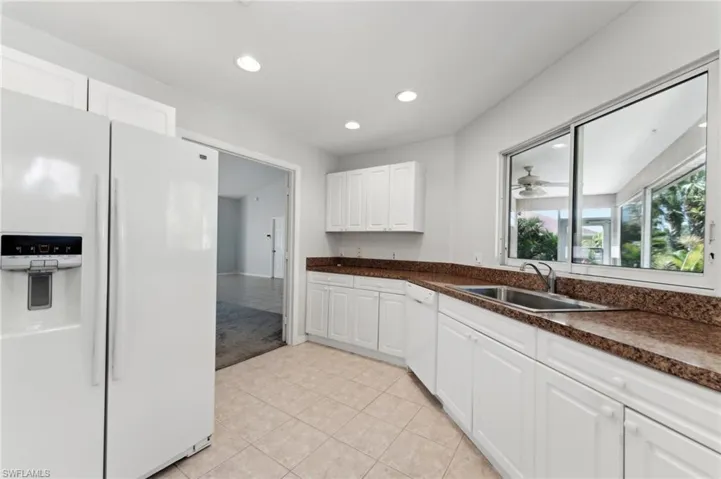 Kitchen with dark countertops, a sink, light tile patterned flooring, white appliances, and recessed lighting