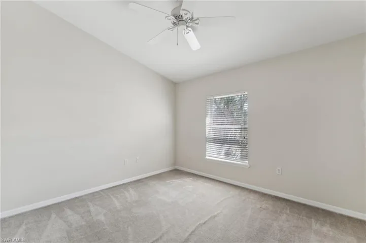 Carpeted spare room with vaulted ceiling, a ceiling fan, and baseboards