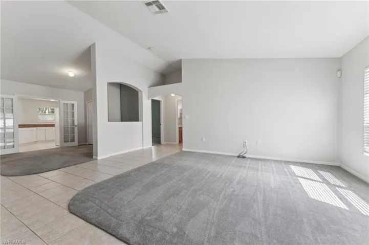 Unfurnished living room with tile patterned floors, arched walkways, vaulted ceiling, visible vents, and baseboards