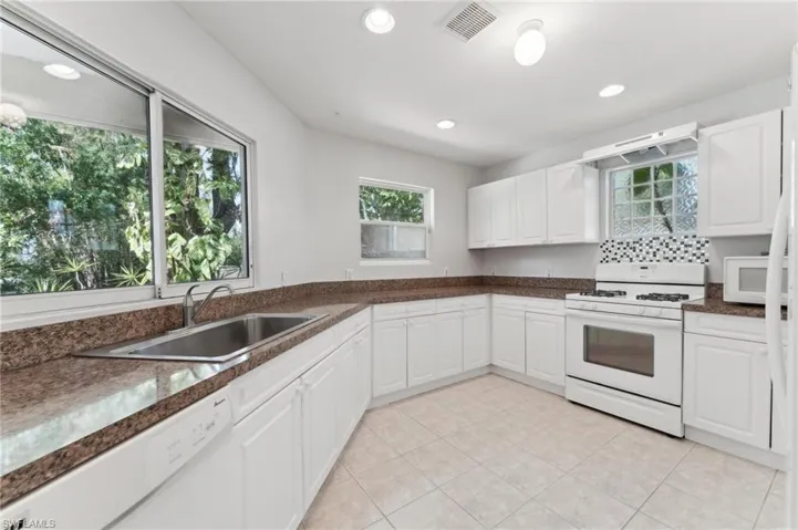 Kitchen featuring recessed lighting, dark countertops, visible vents, a sink, and white appliances
