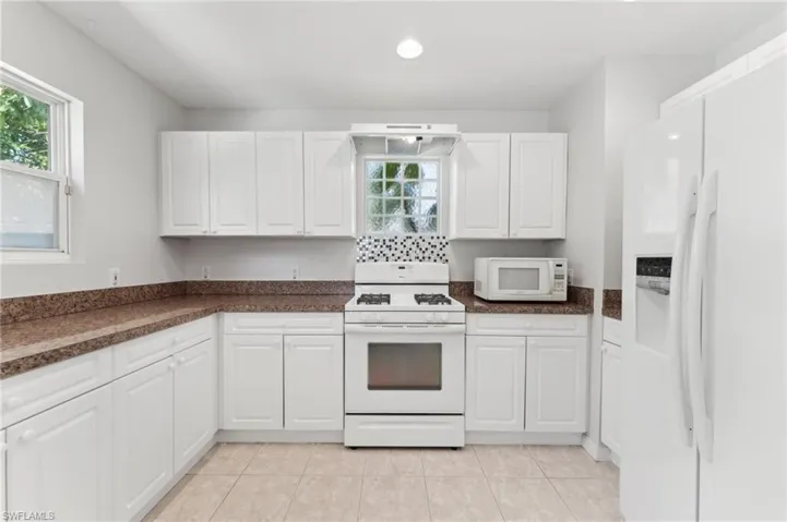 Kitchen with white cabinets, white appliances, and light tile patterned floors