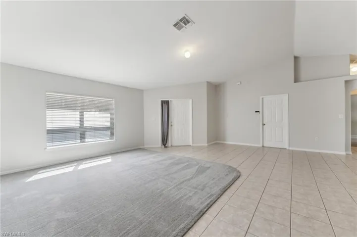 Unfurnished living room with lofted ceiling, baseboards, visible vents, and light tile patterned floors
