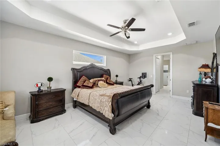 Primary Bedroom with sitting area featuring a tray ceiling, light marble finish flooring, a ceiling fan, and recessed lighting