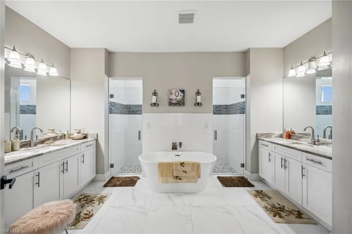 Bathroom with a Walk-In shower, a soaking tub, two vanities, and light marble finish floors
