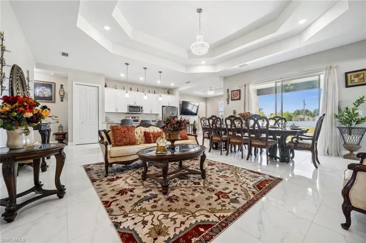Living room with a raised ceiling, light marble finish floors, and recessed lighting