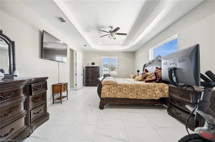 Primary Bedroom with sitting area fearturing a raised ceiling, light marble finish flooring, and ceiling fan