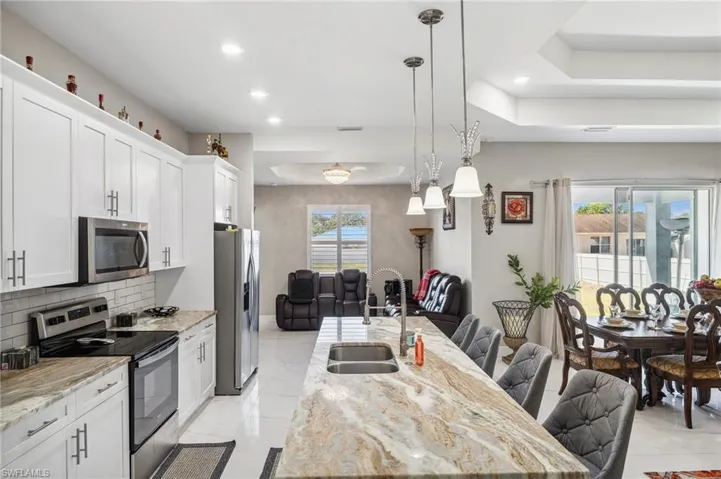 Kitchen with appliances with stainless steel finishes, light stone counters, hanging light fixtures, open floor plan, and recessed lighting