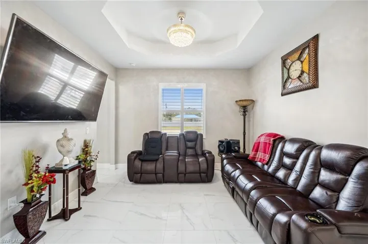 Media Area featuring a tray ceiling, marble finish flooring, and a chandelier