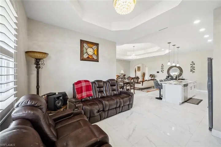Media area with a tray ceiling, arched walkways, light marble finish floors, and a chandelier