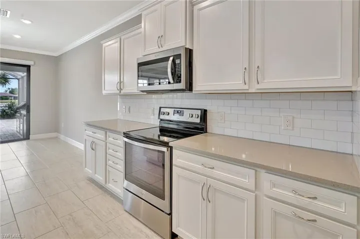 Kitchen with crown molding, baseboards, appliances with stainless steel finishes, and tasteful backsplash