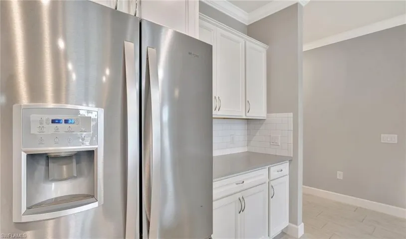 Kitchen featuring white cabinets, stainless steel fridge with ice dispenser, light countertops, backsplash, and ornamental molding