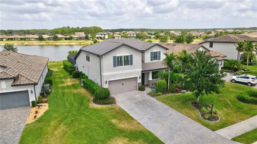 Traditional-style house featuring a front yard, a residential view, decorative driveway, a water view, and stucco siding