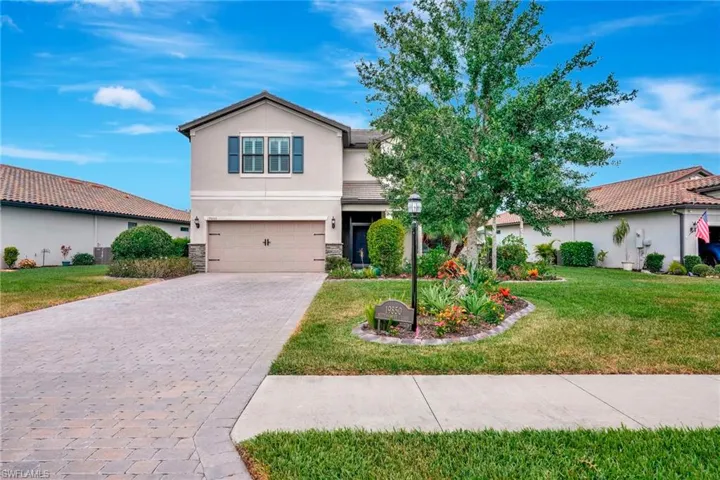 Traditional home with stone siding, a garage, stucco siding, a front yard, and decorative driveway
