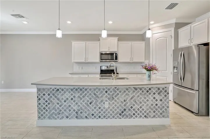 Kitchen with appliances with stainless steel finishes, ornamental molding, a sink, and visible vents