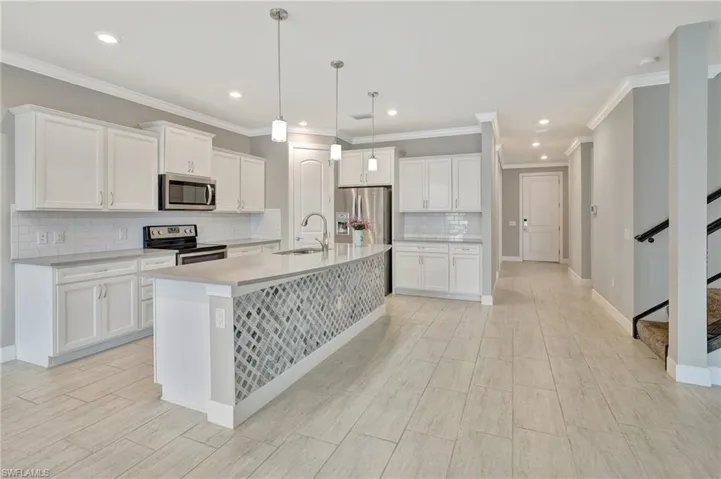 Kitchen featuring decorative backsplash, a center island with sink, white cabinets, a sink, and appliances with stainless steel finishes