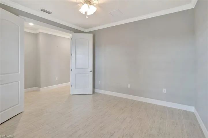Empty room featuring crown molding, light wood finished floors, a ceiling fan, baseboards, and visible vents