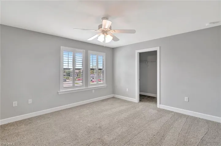 Unfurnished bedroom featuring baseboards, a ceiling fan, carpet floors, and a walk in closet