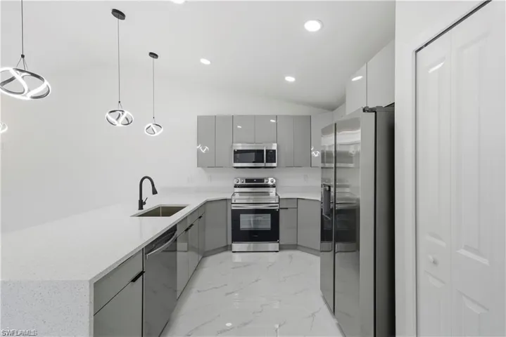 Modern kitchen featuring gray flat-panel cabinetry, stainless steel appliances, white countertops, and contemporary pendant lighting