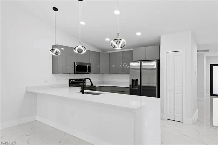 Modern kitchen featuring a large island with an undermount sink, grey cabinetry, stainless steel appliances, white countertops, and contemporary pendant lighting