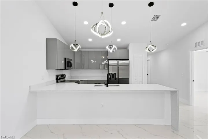 Modern kitchen featuring a large white quartz island, glossy gray cabinetry, stainless steel appliances, and contemporary pendant lighting