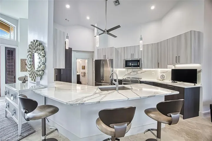 Kitchen featuring a towering ceiling, a breakfast bar area, hanging light fixtures, a ceiling fan, and appliances with stainless steel finishes