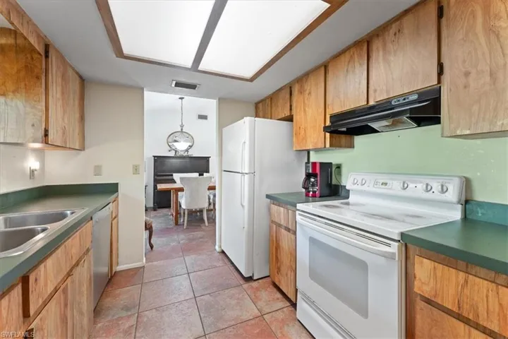 Kitchen with visible vents, under cabinet range hood, light tile patterned floors, white appliances, and a sink