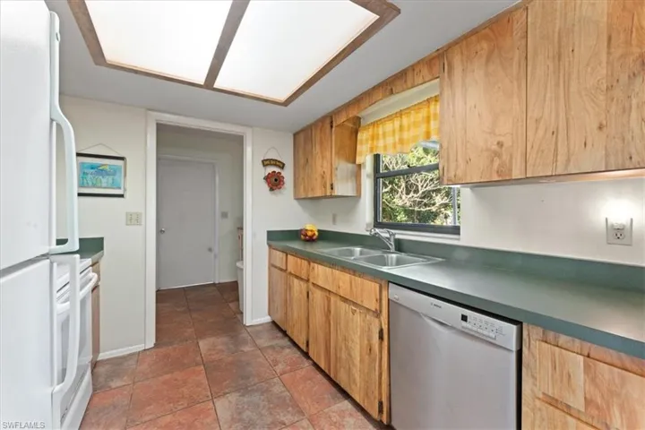 Kitchen with baseboards, freestanding refrigerator, a sink, stainless steel dishwasher, and dark countertops