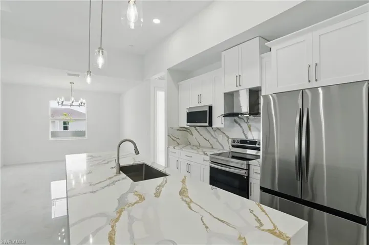 Kitchen featuring appliances with stainless steel finishes, wall chimney range hood, white cabinets, backsplash, and pendant lighting