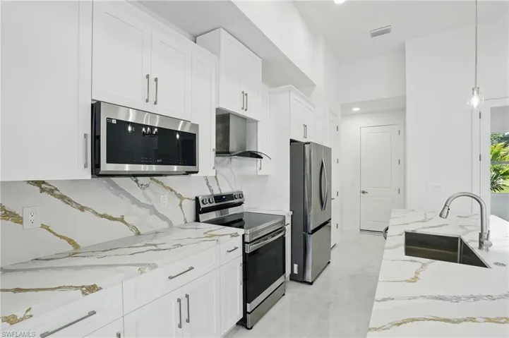 Kitchen with appliances with stainless steel finishes, white cabinetry, light stone countertops, tasteful backsplash, and recessed lighting