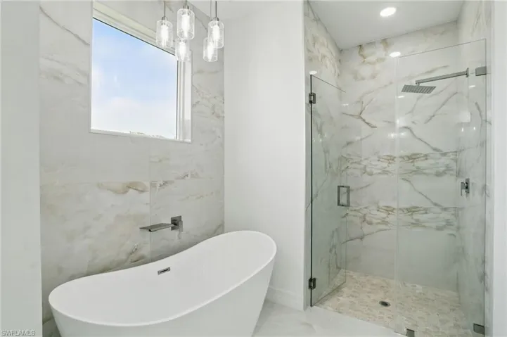 Full bath with a marble finish shower and a soaking tub