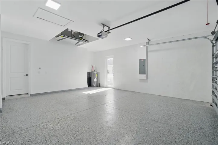 Garage featuring electric water heater, electric panel, and a garage door opener