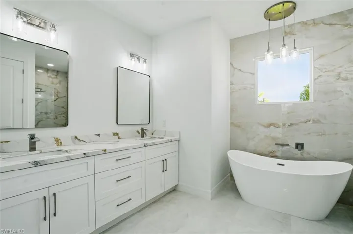 Full bath with marble finish flooring, a freestanding bath, double vanity, and a marble finish shower
