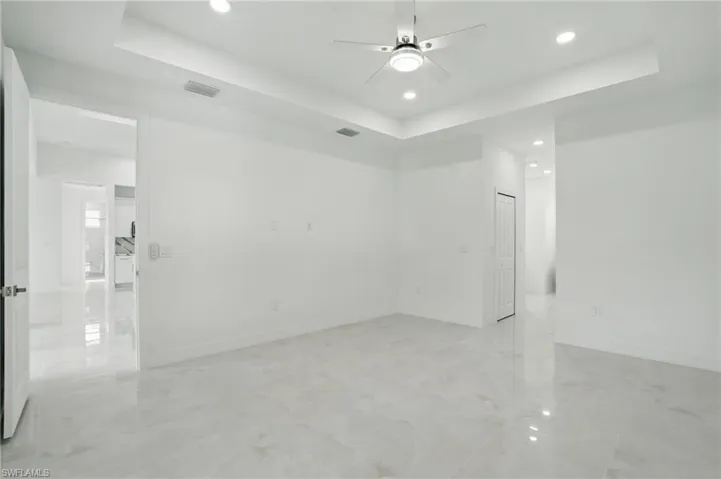 Unfurnished room with a tray ceiling, recessed lighting, a ceiling fan, and light marble finish flooring
