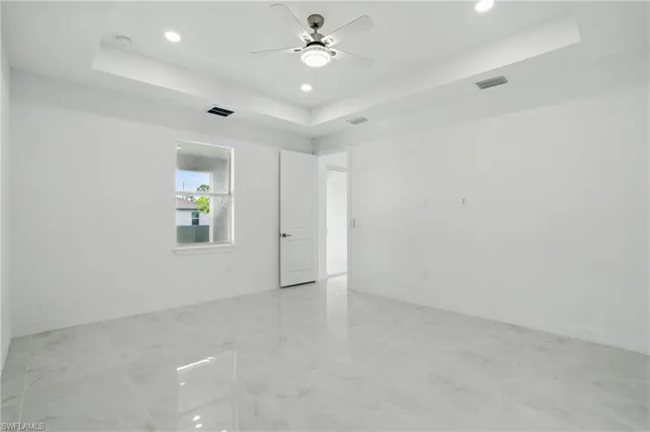 Unfurnished room with a tray ceiling, recessed lighting, a ceiling fan, light marble finish flooring, and a smoke detector