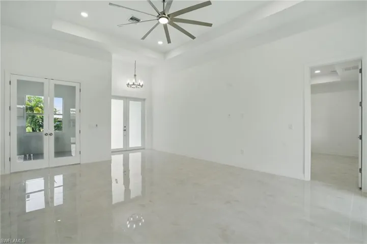 Unfurnished room with french doors, a tray ceiling, a chandelier, recessed lighting, and a ceiling fan