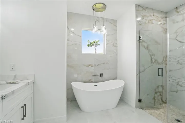 Bathroom featuring marble look tile flooring, a marble finish shower, a freestanding tub, vanity, and a chandelier