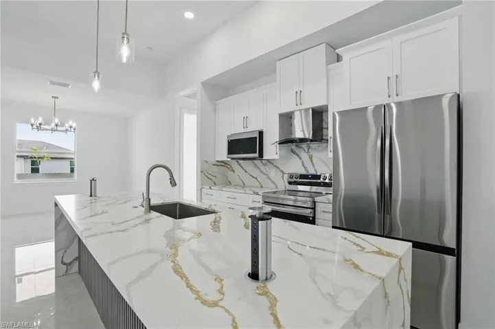 Kitchen featuring stainless steel appliances, wall chimney exhaust hood, a kitchen island with sink, white cabinetry, and backsplash