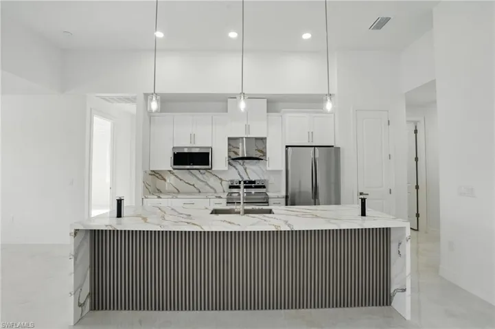 Kitchen featuring stainless steel appliances, white cabinets, tasteful backsplash, a large island with sink, and wall chimney exhaust hood
