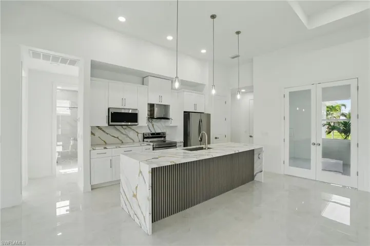 Kitchen with stainless steel appliances, under cabinet range hood, french doors, white cabinets, and recessed lighting