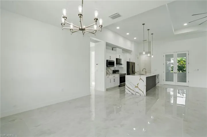 Kitchen featuring appliances with stainless steel finishes, white cabinets, a chandelier, a large island with sink, and hanging light fixtures