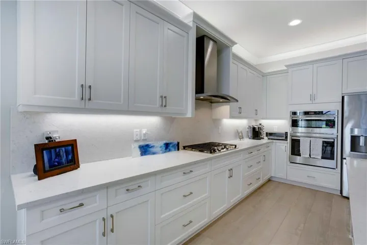 Kitchen with decorative backsplash, light wood-style flooring, wall chimney exhaust hood, and appliances with stainless steel finishes