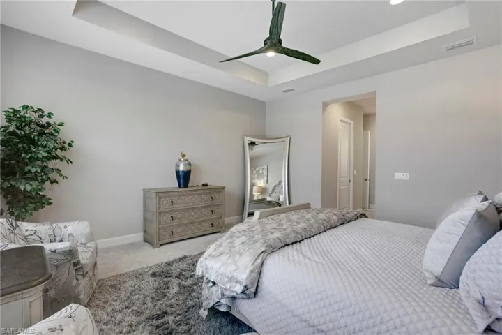 Carpeted bedroom with a raised ceiling, baseboards, ceiling fan, and visible vents