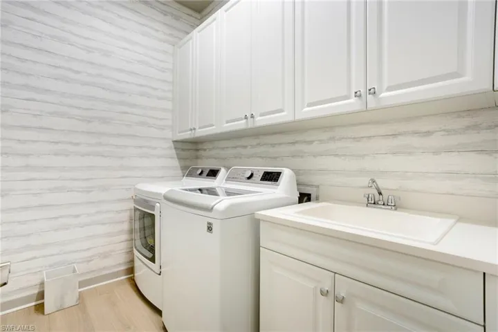 Laundry room with washer and clothes dryer, light wood-style floors, cabinet space, and a sink